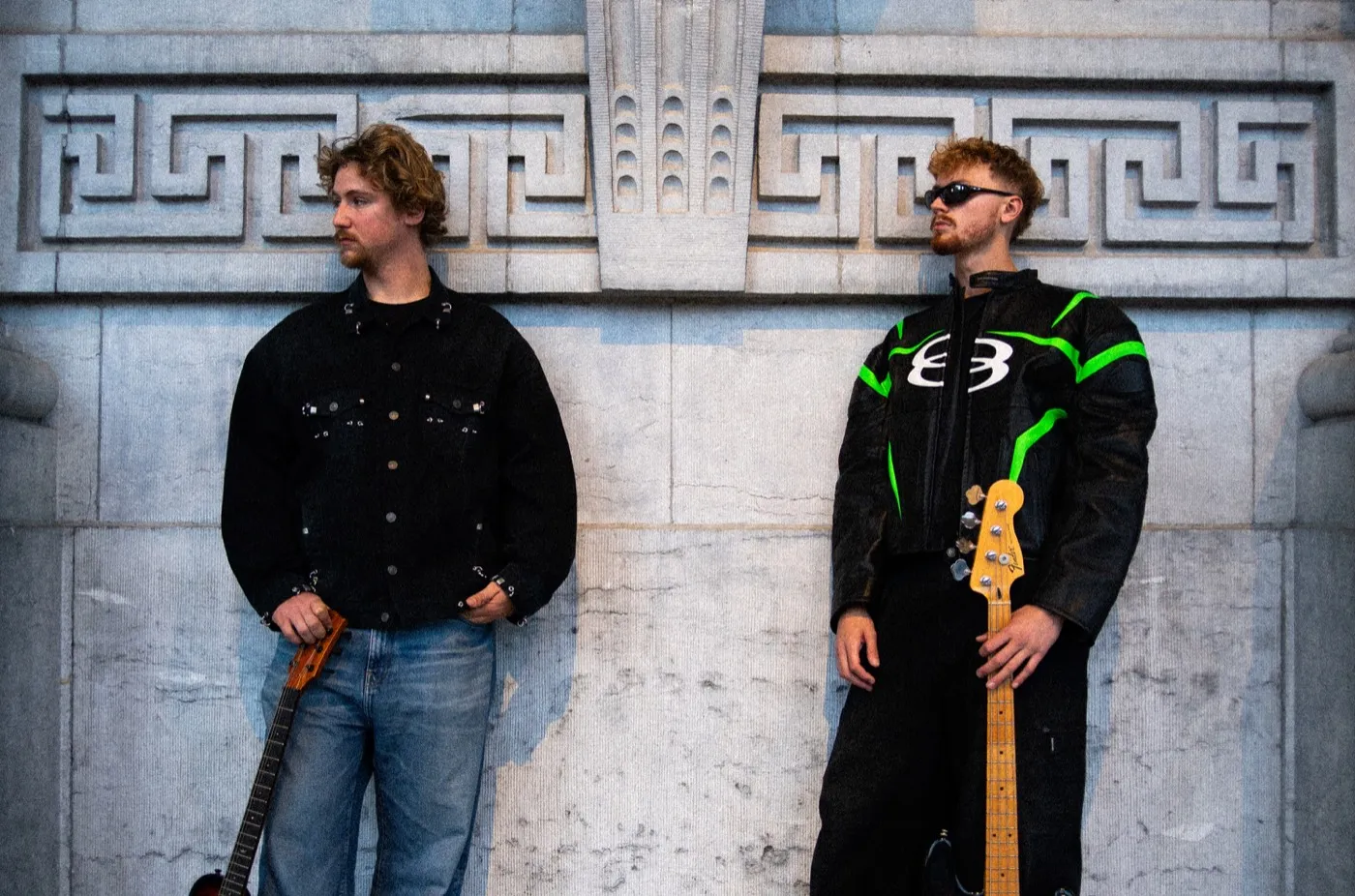 MONOLYTH holding their basses against a wall with Greek key carvings
